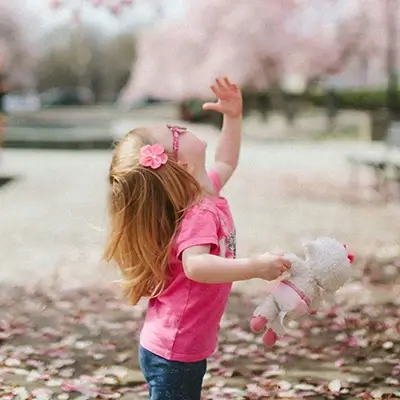 A young girl with pink glasses looks up to the sky while holding a stuffed animal